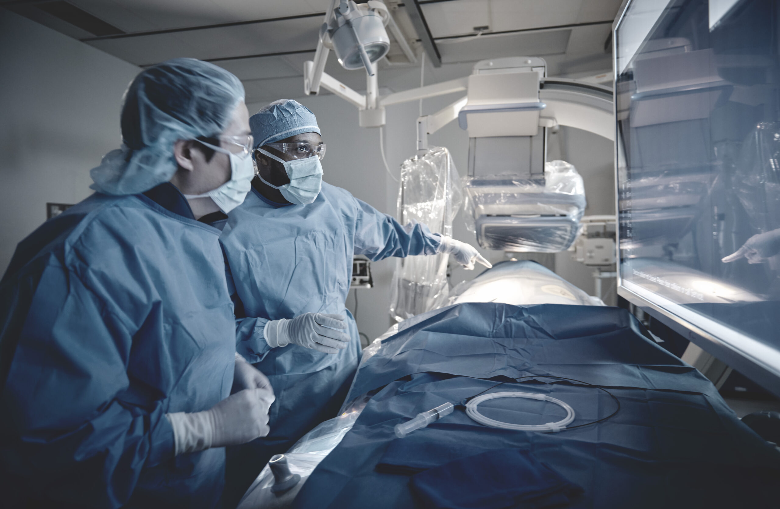Urólogos en un quirófano durante una resección transuretral de próstata, uno operando un resectoscopio y el otro asistiendo, ambos en batas quirúrgicas. Monitores muestran imágenes del procedimiento y signos vitales del paciente, mientras un equipo de enfermeras gestiona el entorno quirúrgico.